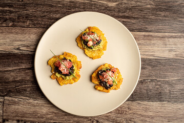 plate of fried patacones with guacamole and beans, on a white plate in a wooden envelope