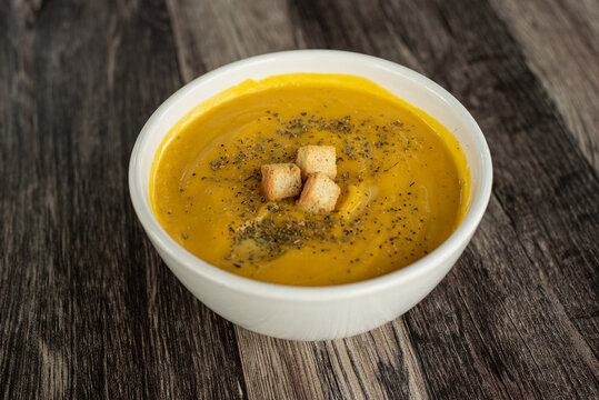 Crema de ayote con crotones, servido en un bowl blanco sobre un fondo de madera. vista superior