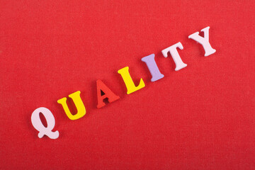 GUALITY word on red background composed from colorful abc alphabet block wooden letters, copy space...