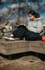 Young girl engrossed in drawing, seated by her bicycle on a bright day in the park, capturing...