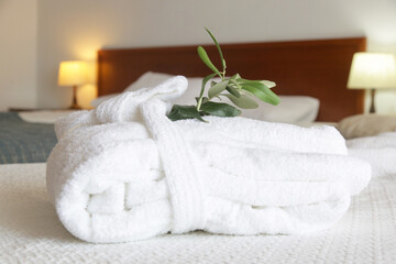 White cotton bathrobe with olive tree twig on the bed  in hotel room. Tourism, hotels, hospitality industry