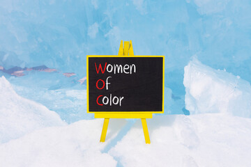 WOC women of color symbol. Concept words WOC women of color on beautiful yellow blackboard. Beautiful blue ice background. Business WOC women of color social issues concept. Copy space. - obrazy, fototapety, plakaty
