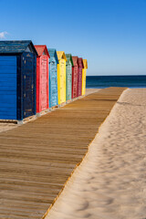 color cabins and huts on a beach with sand, wooden path under blue sky