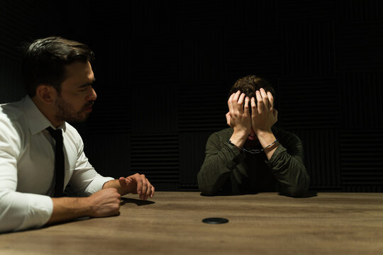 Attorney interviews a handcuffed suspect, exhibiting signs of distress in a dim interrogation room