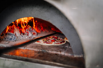 Dobele, Latvia - August 18, 2023 - A pizza with toppings cooking inside a wood-fired oven.