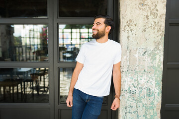 Good looking hispanic man in a white t-shirt ready for branding mock-up, standing outdoors with a joyful expression