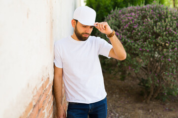 Bearded young hispanic man wearing a blank white t-shirt and cap, ideal for brand mockup designs, standing outdoors
