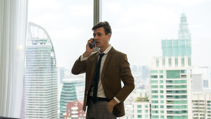 Businessman standing in ornamented office talking on phone with college on cityscape skyline window...