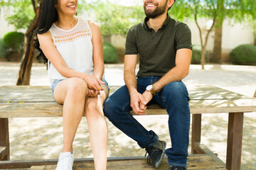 Closeup of a young couple sitting on a bench outdoors, smiling and chatting on a sunny day, exuding...