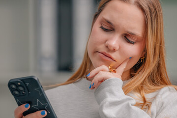 blonde girl at home with mobile phone and doubtful or thoughtful expression