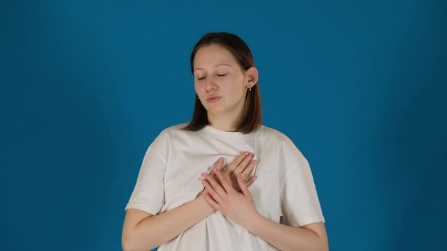 Lady holds hand on chest feeling pain on blue background. Sad woman in T-shirt feels relentless reminder of inner turmoil slow motion