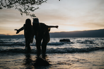 Two girls enjoy a playful moment splashing in the lake water against a scenic sunset backdrop, expressing joy and togetherness.