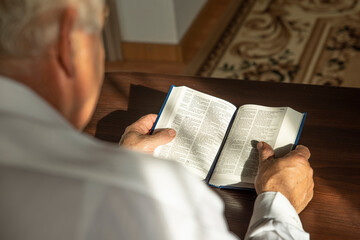 Lifestyle portrait of senior man reading Holy Bible at home. Natural aesthetic light