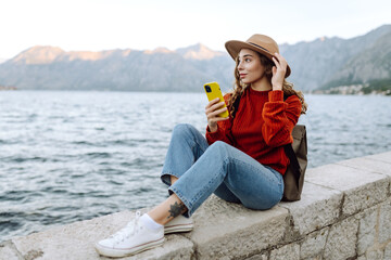 Young woman with phone on the embankment. Tourist during holidays. Lifestyle, travel, nature, active life.