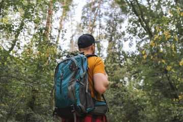 Young male tourist walking in the middle of the early autumn forest with big travel backpack
