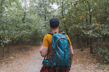Portrait of a young male tourist walking the forest path with big travel backpack