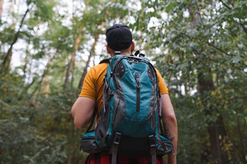 Portrait of a young man tourist walking in the middle of the early autumn forest with big travel backpack
