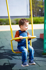 A young boy is sitting on a swing in a park. He is smiling and enjoying himself. The swing is...