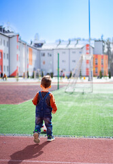 A young boy is walking on a field with a soccer ball in his hand.