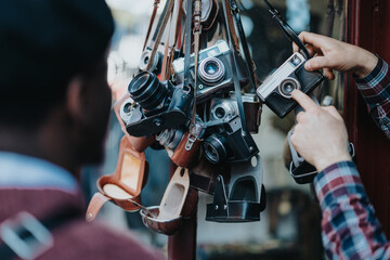 A person picking out a retro camera from a collection of various vintage photography equipment at a street stall. - Powered by Adobe