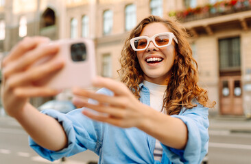 Cheerful female tourist clicking selfie pictures via cellphone front camera. Lifestyle, travel,...