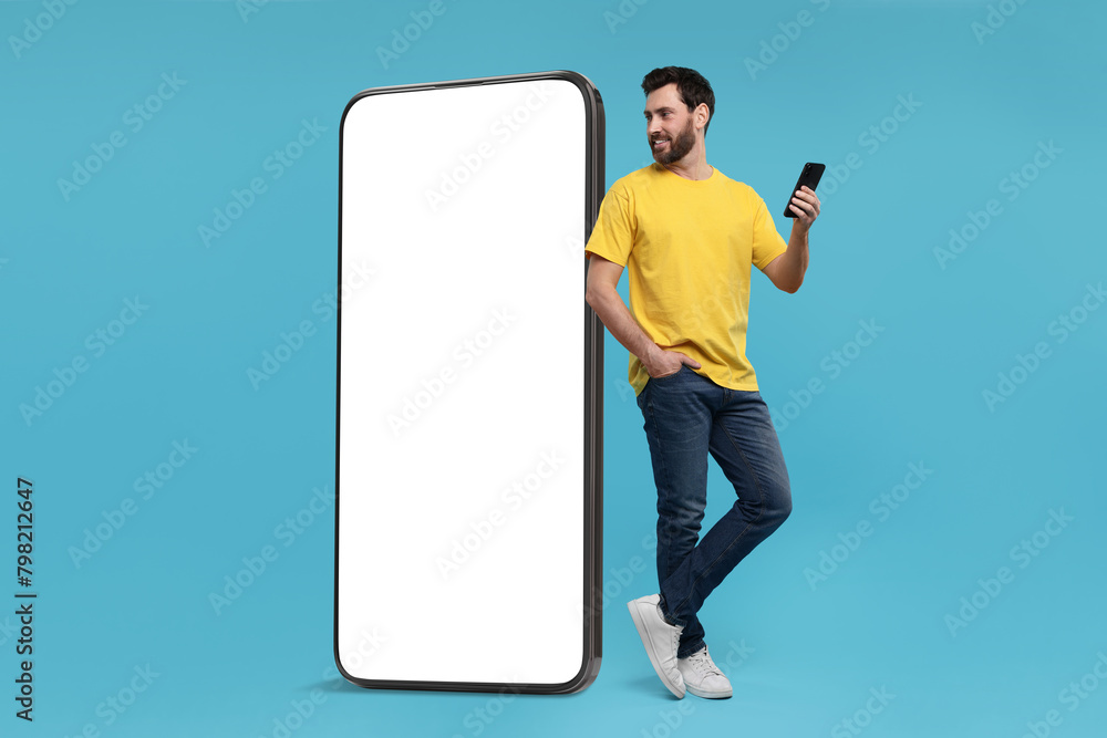 Poster man with mobile phone standing near huge device with empty screen on light blue background. mockup f