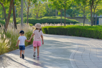 happy boy and girl, brother and sister, walk in the summer sunny park holding hands
