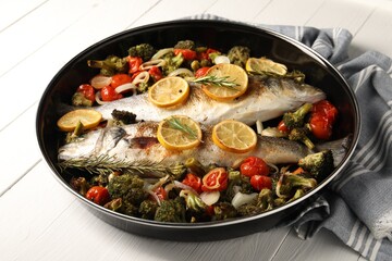 Baked fish with vegetables, rosemary and lemon on white wooden table, closeup