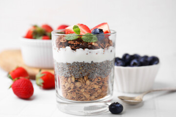 Tasty granola with berries, yogurt and chia seeds in glass on white table