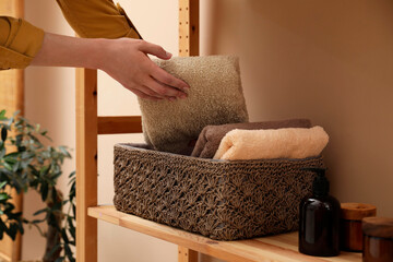 Woman putting towel into storage basket indoors, closeup - obrazy, fototapety, plakaty