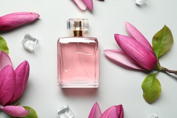 Beautiful pink magnolia flowers, bottle of perfume and ice cubes on light grey background, flat lay