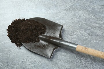 Metal shovel with fertile soil on gray textured surface, top view