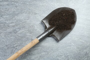 Metal shovel with fertile soil on gray textured surface, above view