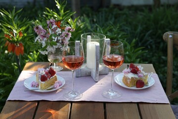Vase with spring flowers, wine and cake on table served for romantic date in garden