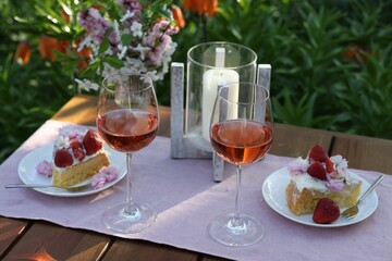 Vase with spring flowers, wine and cake on table served for romantic date in garden