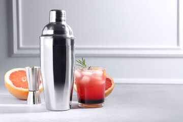 Metal shaker, delicious cocktail, jigger and grapefruit on light grey table, space for text