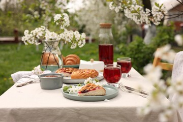 Stylish table setting with beautiful spring flowers, fruit drink and pie in garden