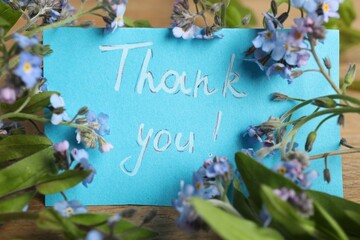 Card with phrase Thank You and beautiful forget-me-not flowers on table, closeup