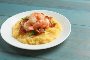 Plate with fresh tasty shrimps, bacon and grits on light blue wooden table