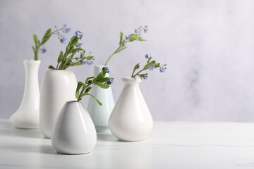 Beautiful forget-me-not flowers in vases on white marble table, closeup. Space for text