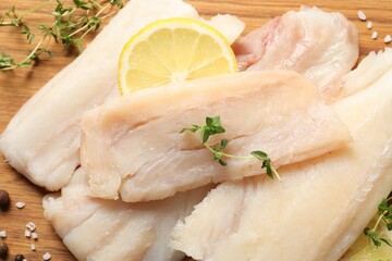 Pieces of raw cod fish and lemon on wooden table, closeup