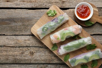 Delicious spring rolls, sauce and chopsticks on wooden table, top view. Space for text