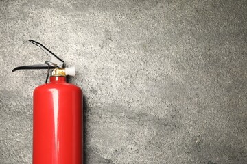 Obraz premium One red fire extinguisher on gray textured background, top view. Space for text