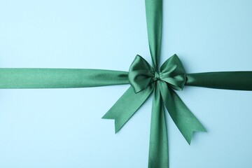 Green satin ribbon with bow on light blue background, top view