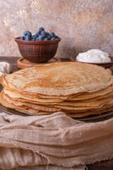A plate of golden pancakes topped with blueberries, accompanied by a bowl of sour cream, a portion of fresh cottage cheese and a glass of milk. On a beige-golden background with a green runner.