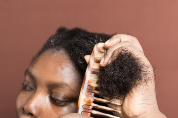 Combing black afro curly hair with shrinkage, using a wide tooth comb to detangle wet Type 4c hair