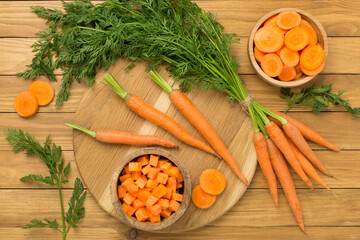 Bunch of fresh carrots with sliced ones on wooden background, top view - obrazy, fototapety, plakaty