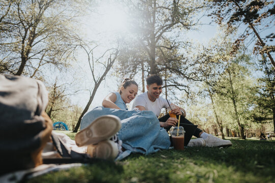 Two students laying on the grass, savoring cold beverages and unwinding in the tranquility of a lush park.