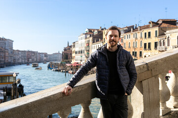 Stylish man in casual wear leaning on the Rialto Bridge in Venice, with the Grand Canal as scenic...