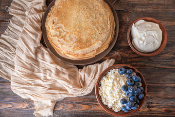 A plate of golden pancakes topped with blueberries, accompanied by a bowl of sour cream, a portion...